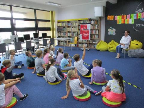 Zdjęcie prezentujące dzieci, uczestników Ogólnopolskiego Dnia Głośnego Czytania w bibliotece gminy Puławy. Pani bibliotekarka czyta przedszkolakom opowiadanie. 