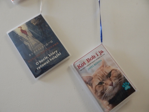 Zdjęcie prezentuje wystawę powieszoną na korytarzu przed biblioteką prezentującą różne okładki książek w których głównym bohaterem jest kot. 