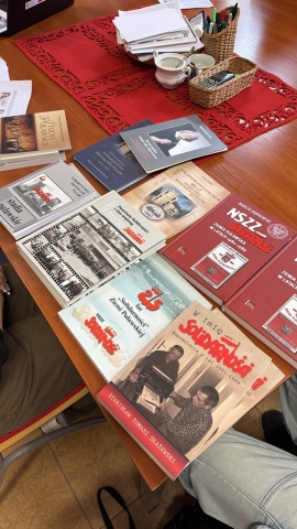 Zdjęcie prezentuje uczniów, którzy uczestniczą w warsztatach edukacyjnych, które dotyczyły historii lokalnej Puław w latach 1917–1990, ze szczególnym uwzględnieniem postaci Marii Kapturkiewicz-Szewczyk i odbyły się 31.03.2026 r. w Powiatowej Bibliotece Publicznej. Na zdjęciu widać ułożone na stole książki poruszające omawianie na warsztatach zagadnienia. 