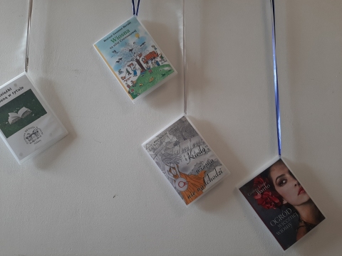 Zdjęcie prezentuje wystawę powieszoną na korytarzu przed biblioteką prezentującą różne okładki książek z wiosną w tytule.