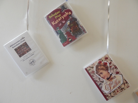 Zdjęcie prezentuje wystawę powieszoną na korytarzu przed biblioteką prezentującą różne okładki książek autorstwa Bolesława Prusa. 