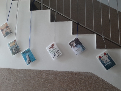 Zdjęcie prezentuje wystawę powieszoną na korytarzu przed biblioteką prezentującą różne okładki książek w których głównym bohaterem jest pies.