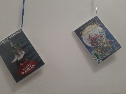 Zdjęcie prezentuje wystawę powieszoną na korytarzu przed biblioteką prezentującą różne okładki książek ze Świętym Mikołajem tytule.