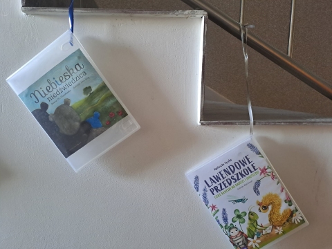 Zdjęcie prezentuje wystawę powieszoną na korytarzu przed biblioteką prezentującą różne okładki książek dla dzieci, w tytule których występuje nazwa jakiegoś koloru.  