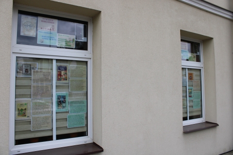 Zdjęcie prezentuje wystawę na oknach Powiatowej Biblioteki Publicznej pokazującą książki dla dzieci, których akcja rozgrywa się właśnie w bibliotece. 