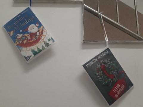 Zdjęcie prezentuje wystawę powieszoną na korytarzu przed biblioteką prezentującą różne okładki książek ze Świętym Mikołajem tytule.
