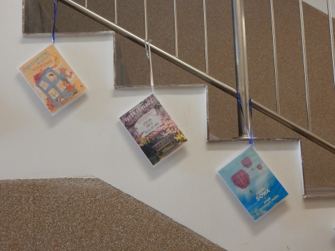 Zdjęcie prezentuje wystawę powieszoną na korytarzu przed biblioteką prezentującą różne okładki książek ze smakiem owoców  tytule.