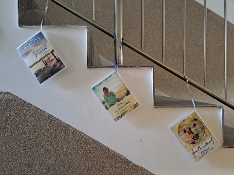 Zdjęcie prezentuje wystawę powieszoną na korytarzu przed biblioteką prezentującą różne okładki książek z wyrazem słońce w tytule.