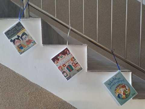 Zdjęcie prezentuje wystawę powieszoną na korytarzu przed biblioteką prezentującą różne okładki książek dla dzieci, w tytule których pojawia się wyraz szkoła. 