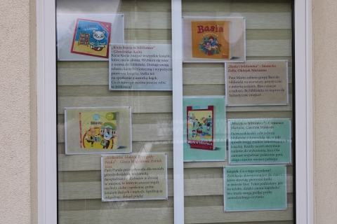Zdjęcie prezentuje wystawę na oknach Powiatowej Biblioteki Publicznej pokazującą książki dla dzieci, których akcja rozgrywa się właśnie w bibliotece. 