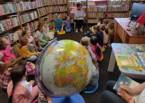 Zdjęcie prezentuje cykl wydarzeń w ramach XXI Tygodnia Bibliotek zorganizowanego przez Bibliotekę Publiczną w Kazimierzu Dolnym: Po niemiecku, hiszpańsku, francusku, włosku, ukraińsku, angielsku … czyta mama i tata”.