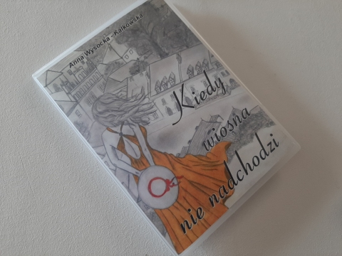 Zdjęcie prezentuje wystawę powieszoną na korytarzu przed biblioteką prezentującą różne okładki książek z wiosną w tytule.