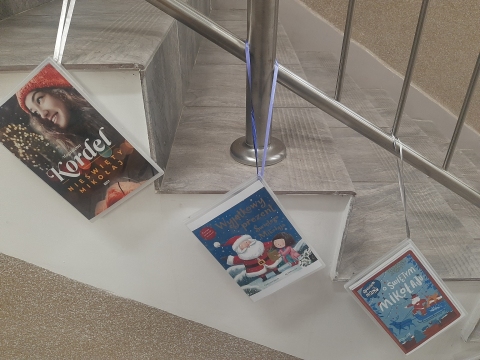 Zdjęcie prezentuje wystawę powieszoną na korytarzu przed biblioteką prezentującą różne okładki książek ze Świętym Mikołajem tytule.