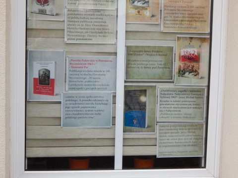 Zdjęcie prezentuje wystawę na oknach Powiatowej Biblioteki Publicznej w Puławach pokazującą różne publikacje dotyczące wybuchu i przebiegu Powstania Styczniowego.