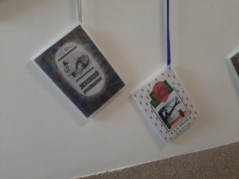 Zdjęcie prezentuje wystawę powieszoną na korytarzu przed biblioteką prezentującą różne okładki książek pt. „Kubuś Puchatek” 