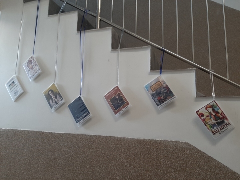 Zdjęcie prezentuje wystawę powieszoną na korytarzu przed biblioteką prezentującą różne okładki książek, w których ważna rolę odgrywają kobiety. 