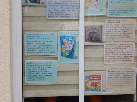 Zdjęcie prezentuje wystawę na oknach Powiatowej Biblioteki Publicznej w Puławach pokazującą książki promujące zdrowe odżywanie wśród najmłodszych. 
