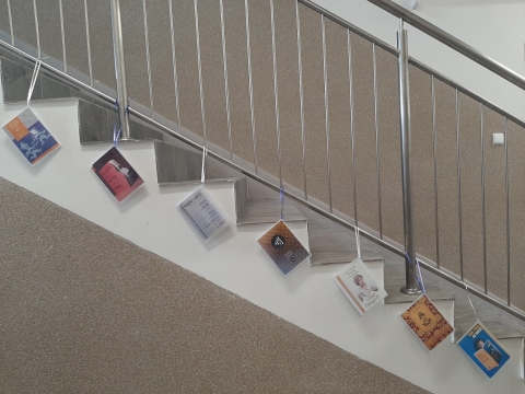 Zdjęcie prezentuje wystawę powieszoną na korytarzu przed biblioteką prezentującą różne okładki książek, w których to właśnie książka jest głównym bohaterem. 