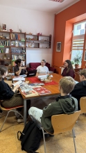 Zdjęcie prezentuje uczniów, którzy uczestniczą w warsztatach edukacyjnych, które dotyczyły historii lokalnej Puław w latach 1917–1990, ze szczególnym uwzględnieniem postaci Marii Kapturkiewicz-Szewczyk i odbyły się 31.03.2026 r. w Powiatowej Bibliotece Publicznej. Na zdjęciu widać siedzących przy stole uczniów klasy 7 i 8 z SP nr 10 i panią Justynę Chabros. 