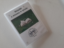 Zdjęcie prezentuje wystawę powieszoną na korytarzu przed biblioteką prezentującą różne okładki książek z wiosną w tytule.