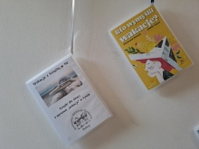 Zdjęcie prezentuje wystawę powieszoną na korytarzu przed biblioteką prezentującą różne okładki książek z wyrazem wakacje w tytule.