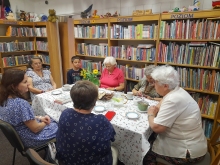 Zdjęcie prezentuje lipcowe spotkanie kazimierskiego DKK, które odbyło się 16 lipca 2026 r. Na zdjęciu kierownik biblioteki Anna Piłat i uczestnicy spotkania: sześć pań i jeden chłopiec. 
