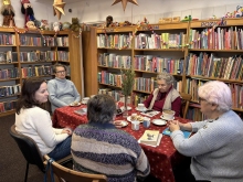 Zdjęcie prezentuje styczniowe spotkanie kazimierskiego DKK, które odbyło się 15 stycznia 2026 r. w siedzibie kazimierskiej biblioteki. Przy stole siedzi pięć pań, które rozmawiają o książce Mariana Pilota pt. „Pantałyk”.